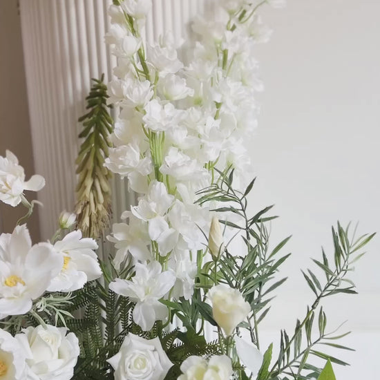 180 degree view of faux floral arrangement on the ground and top of plinths all in white