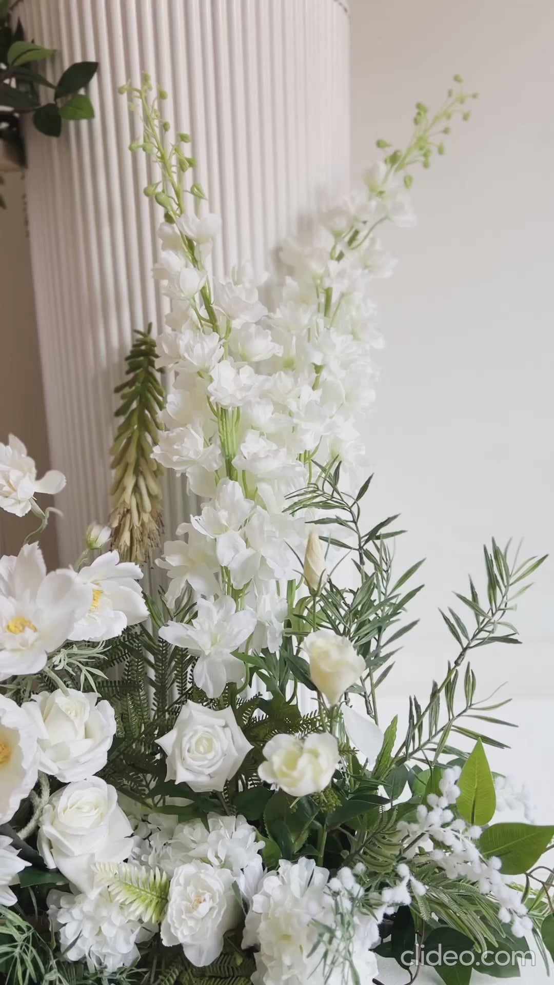 180 degree view of faux floral arrangement on the ground and top of plinths all in white